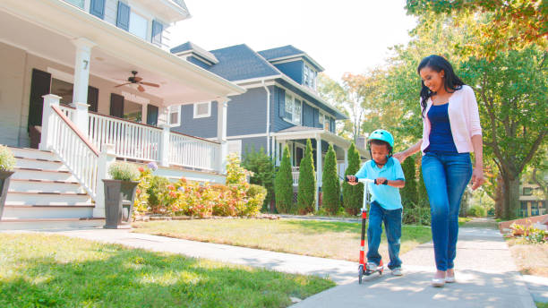 istock Mother Walks With Son As He Rides Scooter Along Sidewalk 2172536256