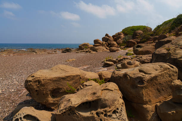 A serene coastal landscape featuring rocky shores and calm waters, framed by lush green hills and distant mountains under a cloudy sky. Ideal for nature and travel themes