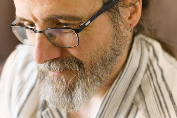 A man with glasses and a beard is thoughtful and smiling. He seems to be remembering something nostalgically