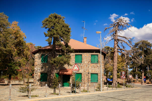 A charming stone building stands in Cyprus, surrounded by trees under a bright blue sky. The greenery and sunny weather create a peaceful atmosphere for visitors and locals alike.