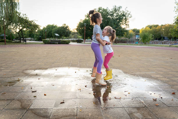 istock Two sisters holding eachother and jumping on a puddle after rain in park 2172551021
