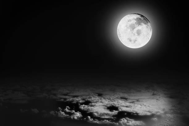 Dramatic image of bright full moon in the night sky background over the white soft clouds. Image use for meteorology and science presentation background. Moon image furnished by NASA.