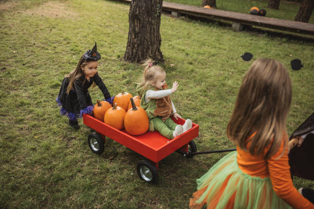 Kids and parents at Halloween backyard party. Pulling cart with pumpkins and having fun.