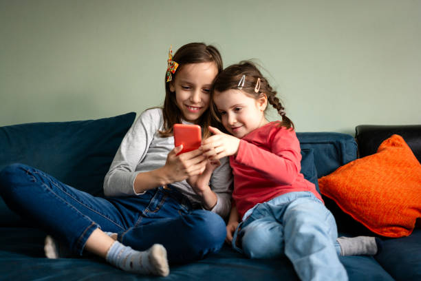 istock Happy girls sitting on sofa and using mobile phone 2172558674