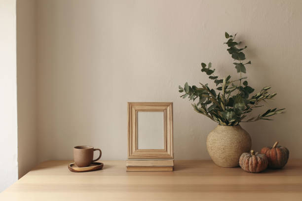 istock Autumn interior still life. Vase with olive eucalyptus tree branches, pumpkins. Blank wooden photo frame mockup on table. Thanksgiving decor. Scandi interior. Cup of tea, coffee. Beige wall background 2172558681