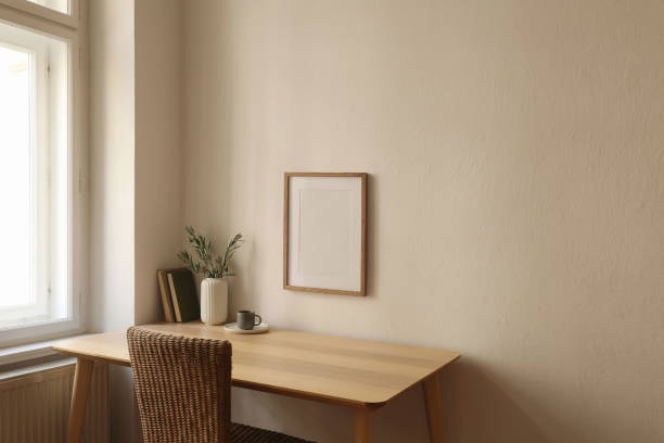 istock Modern vase with olive branches, old books. Blank vertical wooden picture frame mockup on wall. Home office table near window. Minimal Scandi boho interior. Cup of tea, coffee. Beige wall background. 2172558689