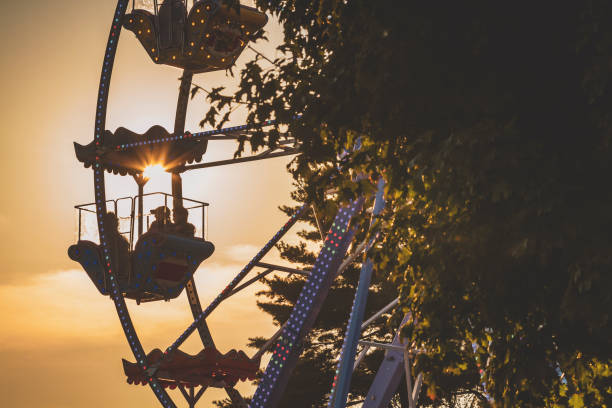 istock Silhouette of people sitting inside a ferris wheel against the setting sun. 2172560164