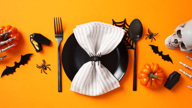 istock Halloween table setting with napkin on black plate, cutlery, spooky decorations, pumpkins on orange background. Flat lay, top view. 2172560350