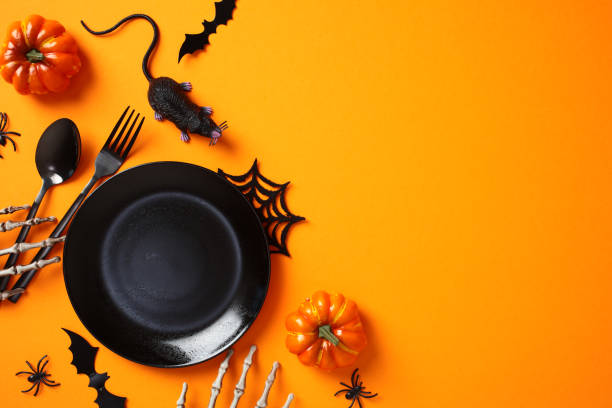 istock Halloween table setting. Flat lay composition with black empty plate, cutlery, pumpkins, Halloween decor on orange background. 2172560560