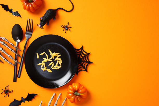 istock Halloween table setting. Flat lay composition with maggots in black plate, cutlery, pumpkins, scary decorations on orange background 2172560623