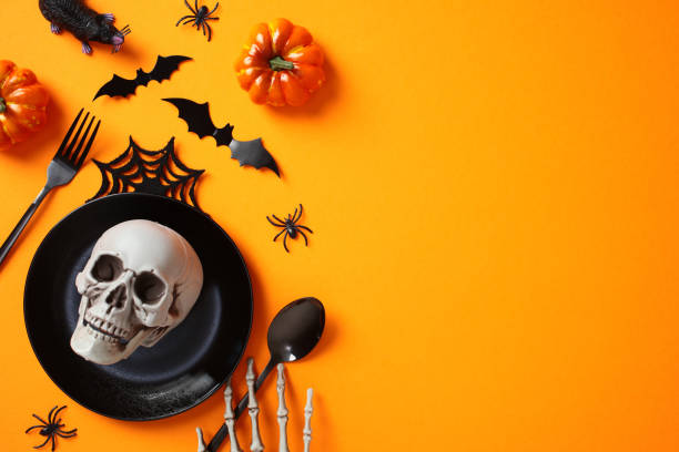 istock Scary Halloween table setting. Top view skull in black plate, cutlery, Halloween decorations, pumpkins on orange background. 2172560692