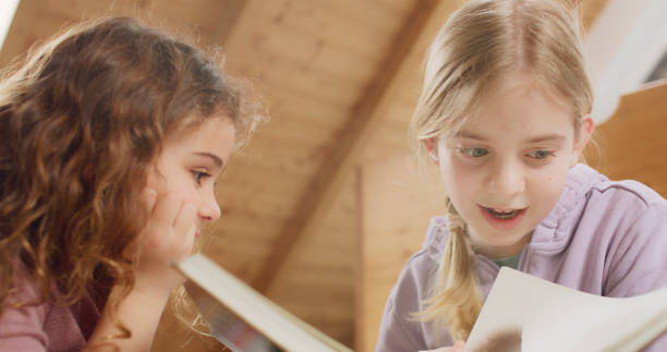 Low angle view of smiling girl listening to her sister reading book at home.