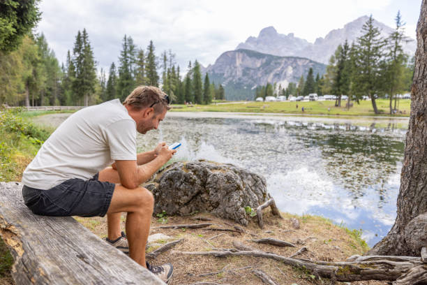 istock Man Sitting by a Lake Using Smartphone in Scenic Mountain Landscape 2172575702