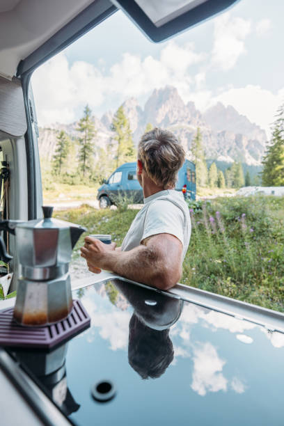 istock Man Smiling While Enjoying Coffee Outside Campervan in Mountain Landscape 2172582822