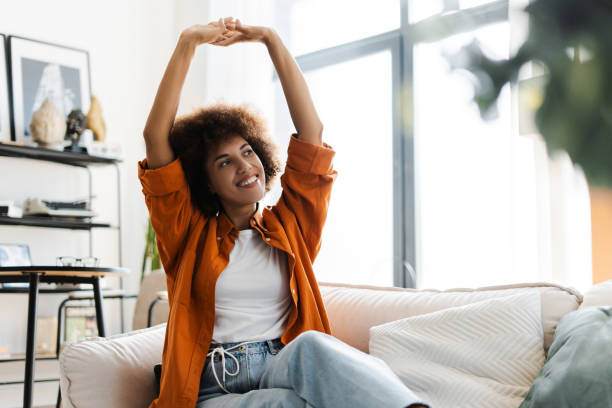 istock Smiling active woman stretching hands, doing exercises sitting on sofa relaxing at home 2172585317