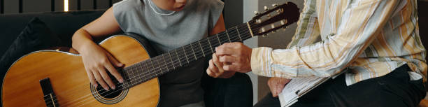 African American guitarist performing on acoustic instrument while sound engineer documents recording process in professional studio setting