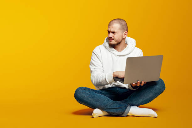istock Thoughtful man sitting on floor and holding laptop computer while looking at empty space for text 2172591343