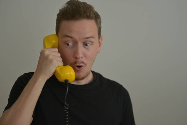 A man talking on the phone with a yellow retro telephone receiver. Emotion expression of surprise astonishment concept. Emotional reaction from the conversation. Banner background with copy space.