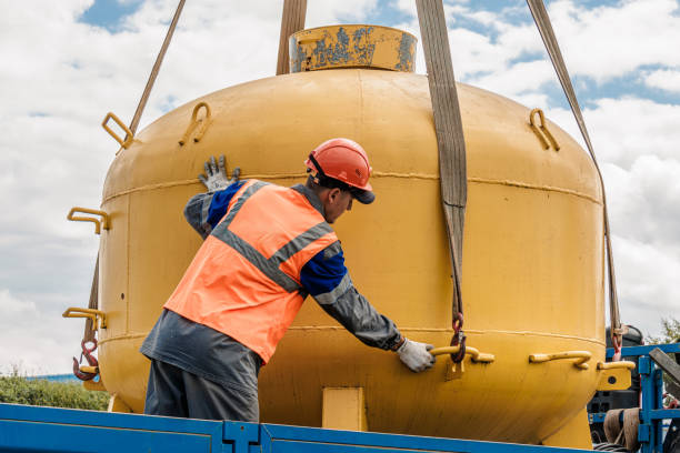 istock Manual laborer adjusting straps on a large yellow tank during a lifting operation. 2172591488