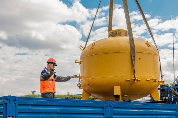 Worker securing a large yellow industrial tank with a crane on a sunny day.