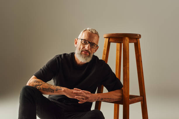 istock Emotionally expressive mature man seated beside a wooden stool on a vibrant backdrop 2172597968