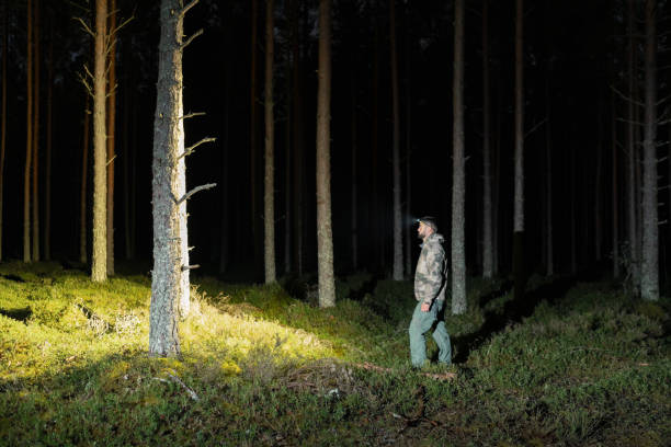 istock A man in camouflage, a volunteer searcher, with a flashlight in a pine forest at night. 2172606039