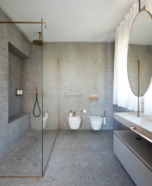 Modern bathroom with large granite slabs, both on the walls and on the floor. Front view of toilet, bidet and large open glass shower. No one inside