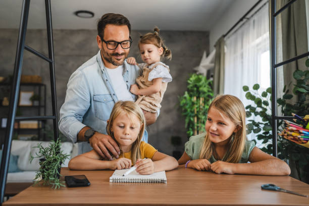 istock single father hold youngest daughter while other daughters do homework 2172622206