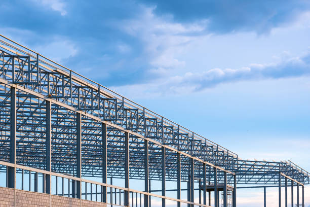 Factory building structure with gray metal columns and roof beam outline in construction site against blue sky background, perspective side view with copy space