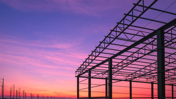 istock Silhouette industrial warehouse building structure with metal framework in construction site and row of electric poles against colorful twilight sky background 2172624484