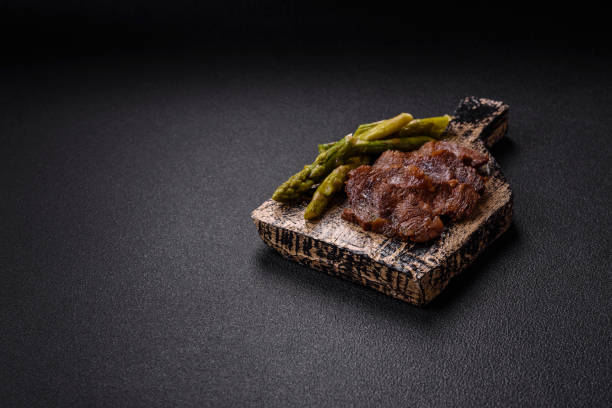 Juicy beef or pork cut into slices with boiled asparagus, salt and spices on a dark concrete background