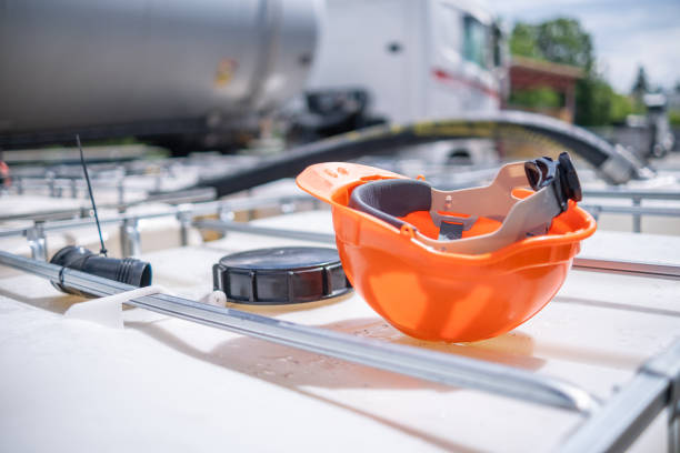 A 1000 liter IBC bulk container with safety gloves and helmet on them. During workers' rest. In the background other containers and a tank truck.
