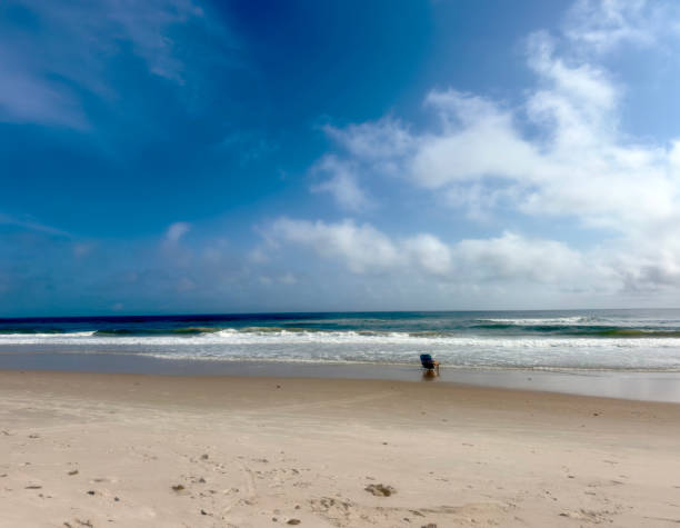 A pair of blue beach chairs with umbrellas sitting on white sandy beaches in front of the ocean on a sunny day.