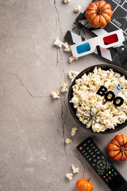 Halloween-themed vertical setup with popcorn, mini pumpkins, 3D glasses, and remote control for a perfect horror movie night ambiance