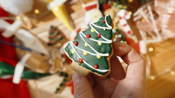 istock Hand Holds a Decorated Christmas Tree Cookie, Surrounded by Various Festive Cookies on a Wooden Board. 2172682840
