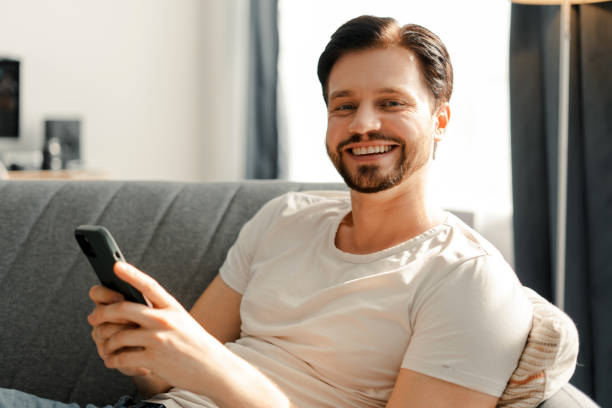 istock Happy man using smartphone relaxing on sofa at home 2172706040