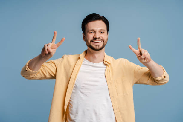 istock Bearded man showing peace sign with both hands is smiling at camera isolated on blue background 2172707462