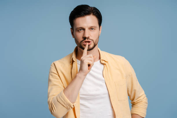 istock Young man making silence gesture with finger on lips looking at camera isolated on blue background 2172707473