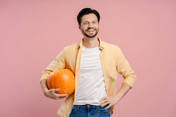 istock Handsome, smiling man smiling and holding a pumpkin on pink background looking at camera 2172707680