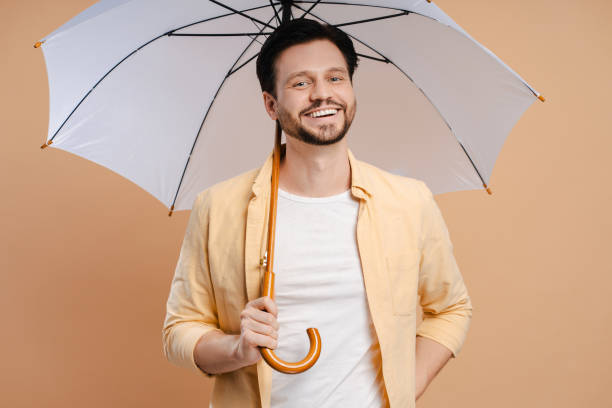 istock Handsome man smiling holding umbrella on beige background 2172707725