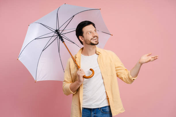 istock Smiling man holding umbrella checking if rain stopped posing on pink background 2172707782