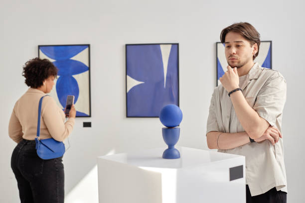 Minimal waist up portrait of thoughtful young man looking at modern art piece while visiting gallery or museum in white and blue colors copy space