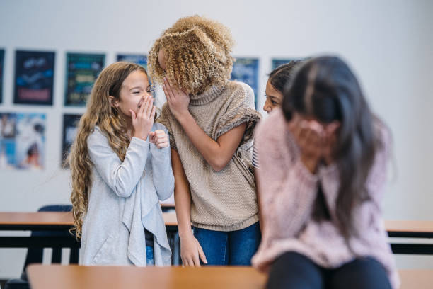 istock An upset girl sits in classroom while her fellow students bully her 2172736864