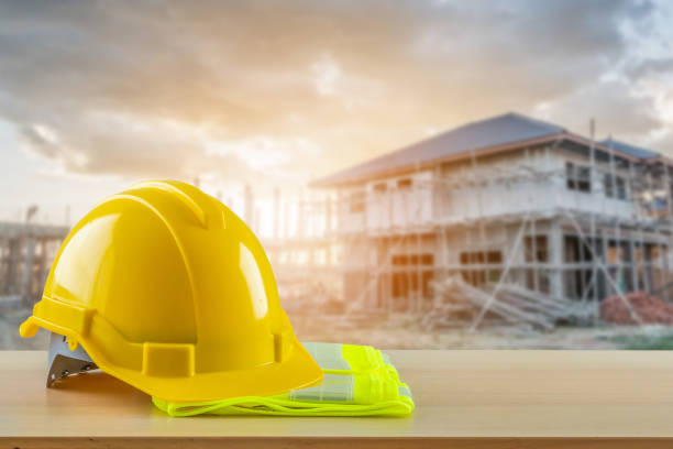 istock Yellow safety construction helmet on wood table with construction site background 2172740791