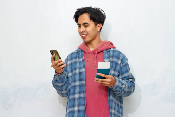 istock Happy young Asian man looking at smartphone while holding passport. Excited expression, modern travel concept. 2172751977