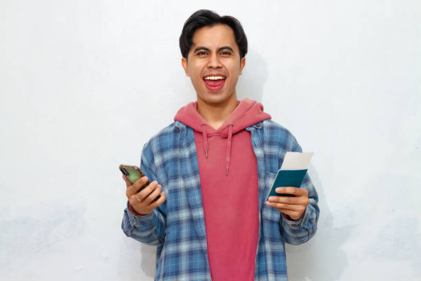 istock Happy young Asian man looking at smartphone while holding passport. Excited expression, modern travel concept. 2172752127