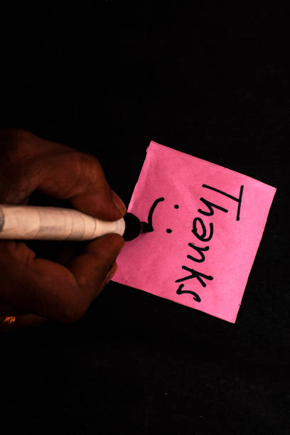 A woman writes the word Thanks on a pink paper note with a black background, leaving empty space for additional text. Perfect for expressing gratitude or appreciation in designs.