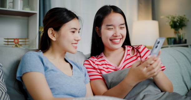 istock Two women are sitting on a sofa and talking while looking at smartphone. 2172762427