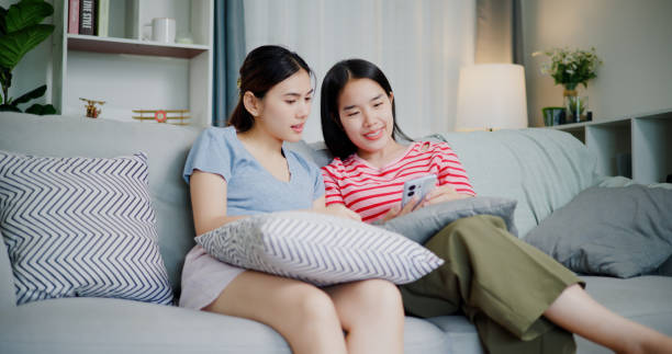 istock Two women are sitting on a sofa and talking while looking at smartphone. 2172762470