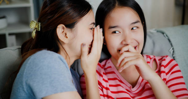 istock Two young women whisper in each other's ears and talk about fun things or make plans together during a peaceful time at home. 2172762478